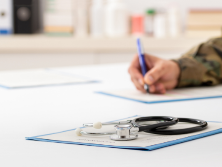 Stethoscope sitting on plan for ongoing veterans health care Darwin and military doctor's hand holding pen writing - Contact VHC today